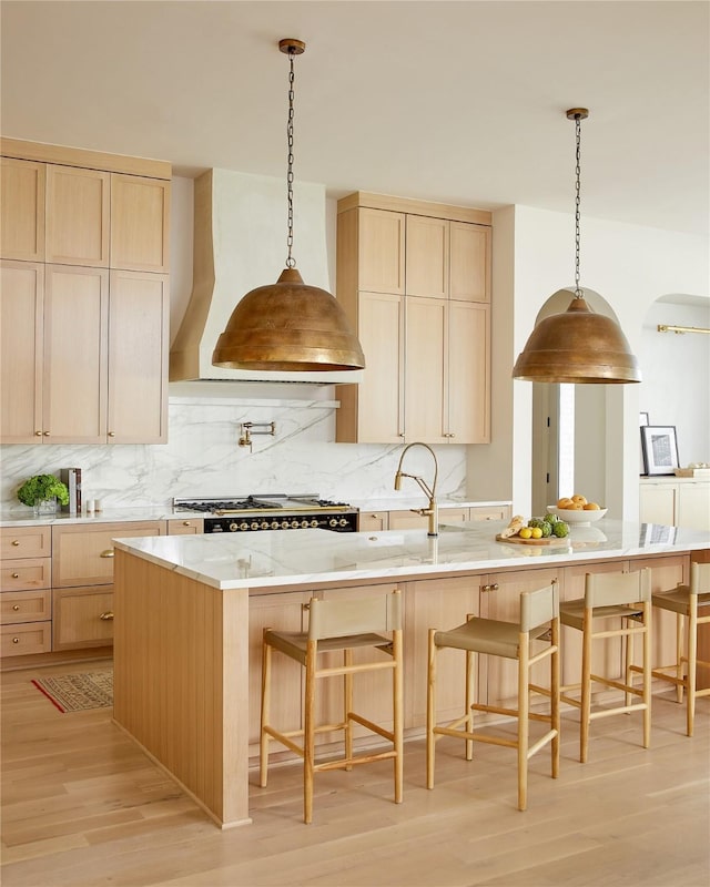 kitchen with light wood-type flooring, premium range hood, backsplash, and light brown cabinetry