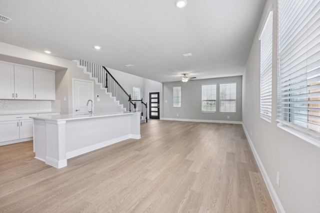 unfurnished living room with light wood-type flooring, recessed lighting, baseboards, ceiling fan, and stairs