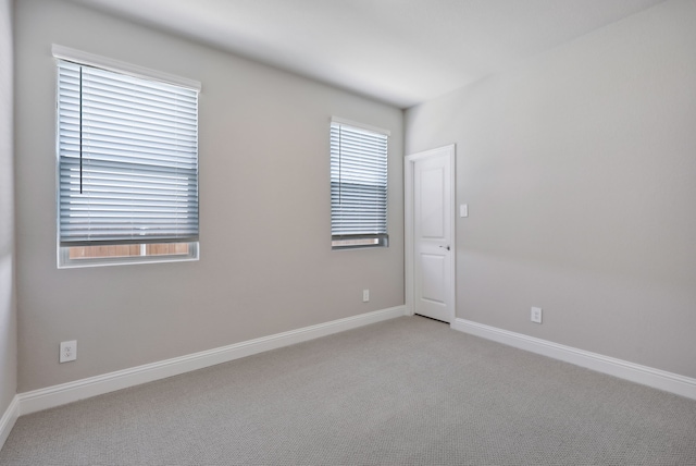 spare room with baseboards and light colored carpet