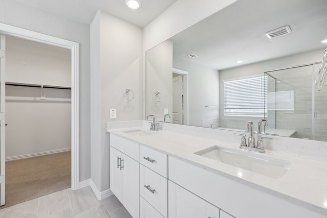 full bath with visible vents, a stall shower, a walk in closet, and a sink