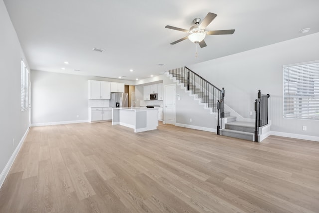 unfurnished living room with recessed lighting, light wood-type flooring, stairs, and baseboards