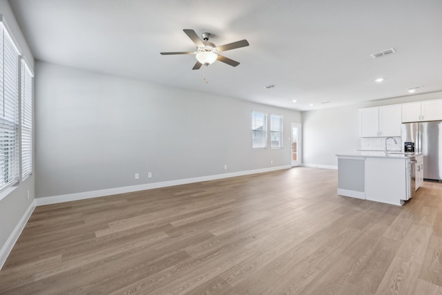 unfurnished living room featuring light wood finished floors, visible vents, ceiling fan, baseboards, and a sink