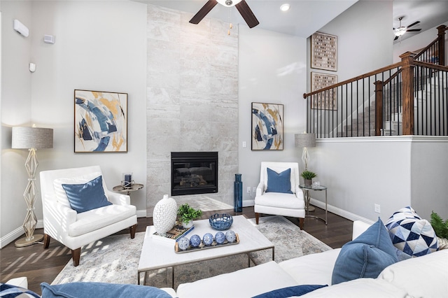 living room featuring a ceiling fan, a tile fireplace, baseboards, and wood finished floors