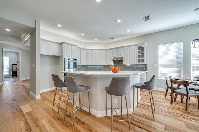 kitchen with under cabinet range hood, a kitchen breakfast bar, decorative backsplash, and light wood finished floors