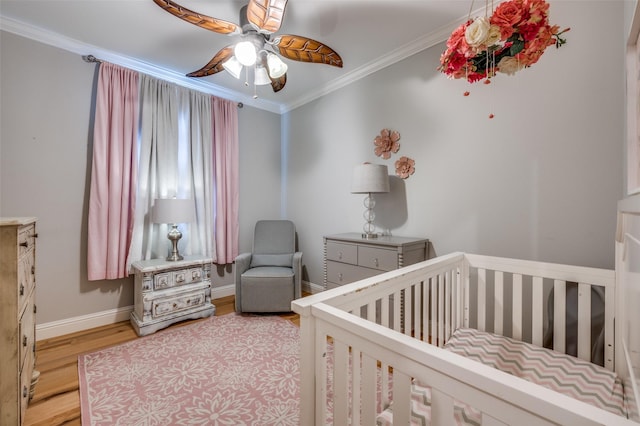 bedroom featuring a crib, light wood finished floors, baseboards, a ceiling fan, and crown molding