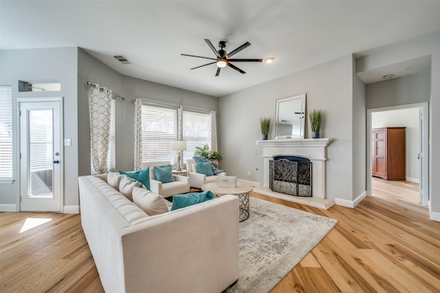 living room with a fireplace with raised hearth, ceiling fan, visible vents, baseboards, and light wood-type flooring