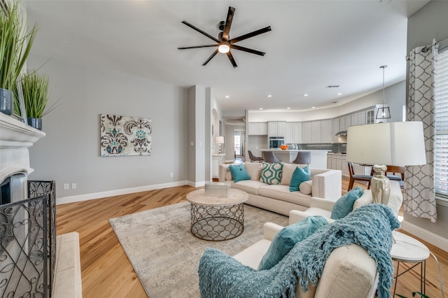 living room featuring a fireplace, recessed lighting, light wood-style floors, a ceiling fan, and baseboards