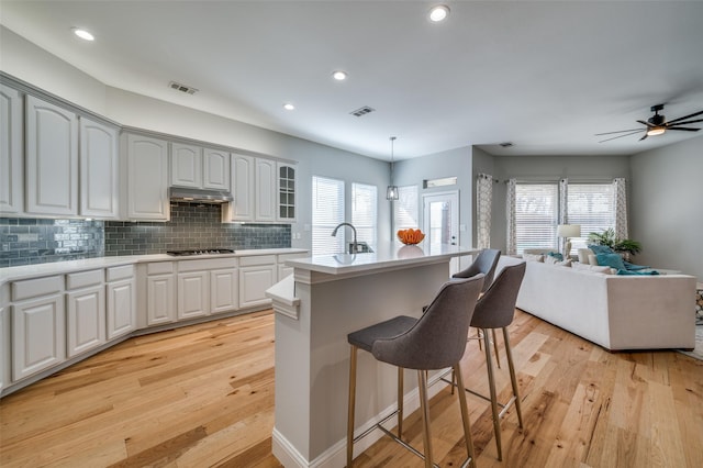 kitchen with open floor plan, under cabinet range hood, light wood-style floors, and a kitchen breakfast bar