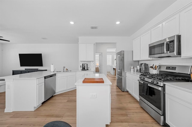 kitchen featuring a center island, visible vents, appliances with stainless steel finishes, a sink, and a peninsula