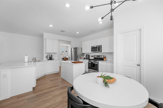 kitchen featuring stainless steel appliances, white cabinetry, light wood-style floors, backsplash, and a center island