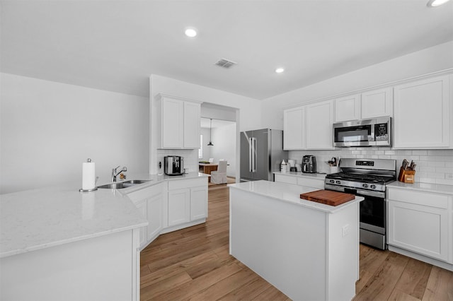 kitchen with stainless steel appliances, light wood-type flooring, a peninsula, and a sink