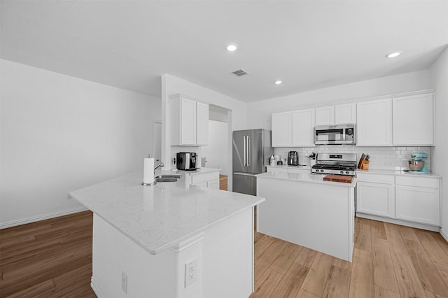 kitchen with a peninsula, visible vents, appliances with stainless steel finishes, backsplash, and light wood finished floors