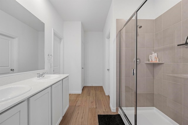 bathroom featuring double vanity, wood finished floors, a stall shower, and a sink