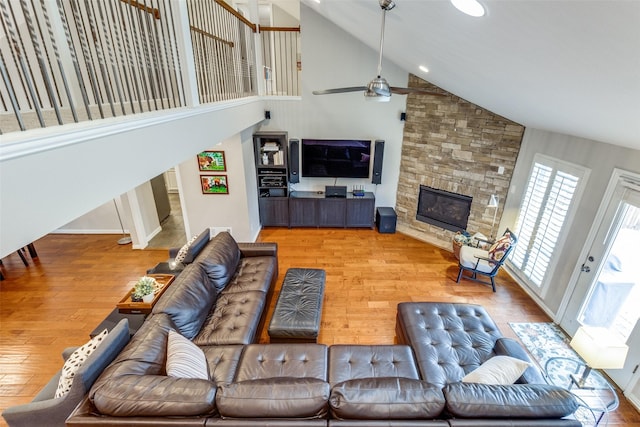 living room with high vaulted ceiling, a stone fireplace, wood finished floors, and a ceiling fan