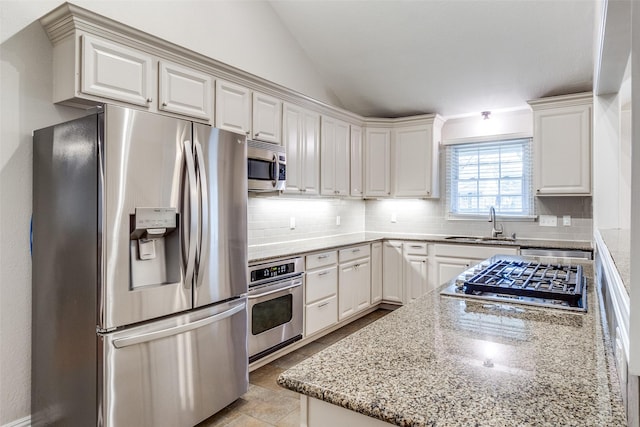 kitchen featuring lofted ceiling, a sink, appliances with stainless steel finishes, decorative backsplash, and light stone countertops