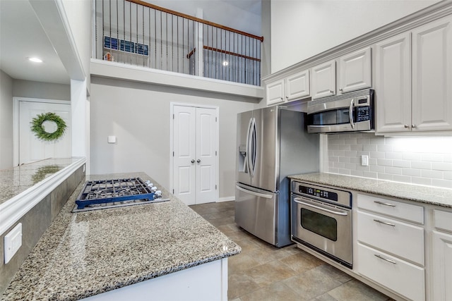 kitchen with appliances with stainless steel finishes, white cabinets, a towering ceiling, and tasteful backsplash