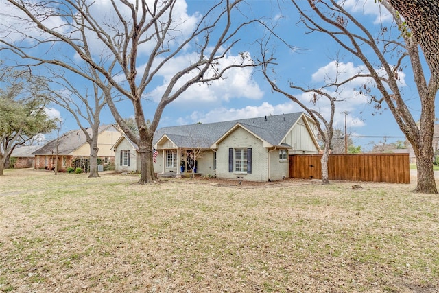 view of front of house with a shingled roof, fence, a front lawn, board and batten siding, and brick siding