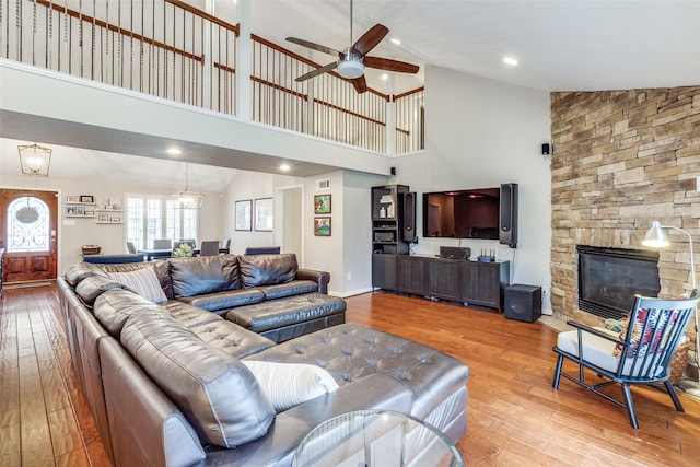 living room with ceiling fan with notable chandelier, a fireplace, lofted ceiling, and hardwood / wood-style flooring