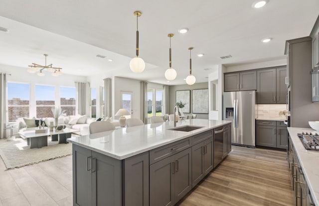 kitchen with gray cabinetry, stainless steel appliances, a sink, tasteful backsplash, and an island with sink