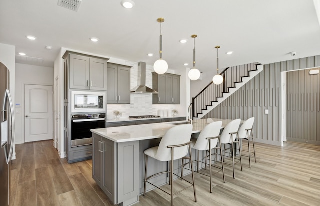 kitchen with wall chimney range hood, stainless steel appliances, visible vents, and gray cabinets