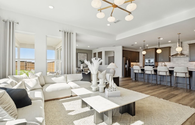 living area featuring light wood-type flooring, visible vents, a notable chandelier, and recessed lighting