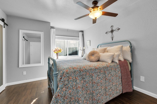 bedroom with ceiling fan, a barn door, wood finished floors, and baseboards