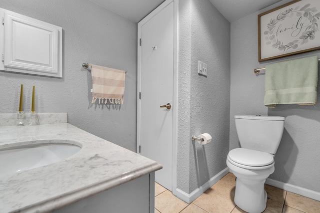 bathroom featuring baseboards, a textured wall, toilet, tile patterned flooring, and vanity