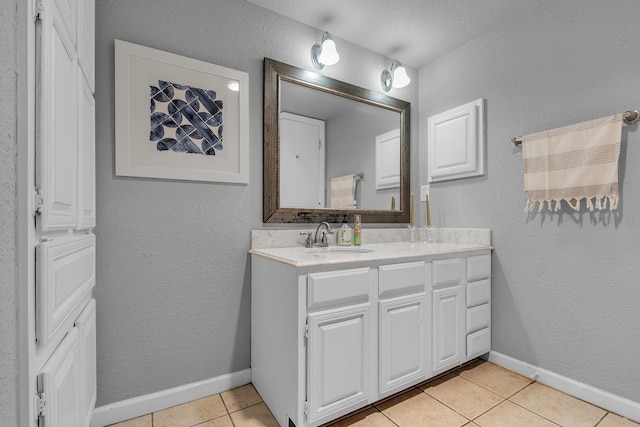 bathroom with a textured wall, vanity, baseboards, and tile patterned floors