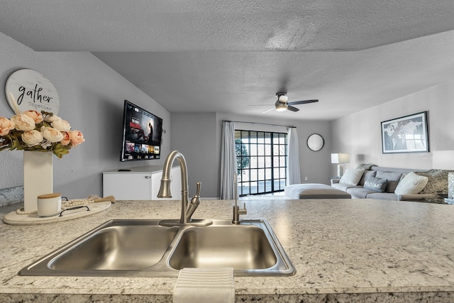 kitchen with light countertops, a ceiling fan, open floor plan, a sink, and a textured ceiling