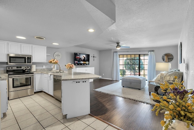 kitchen with appliances with stainless steel finishes, light wood-style floors, open floor plan, white cabinets, and a peninsula