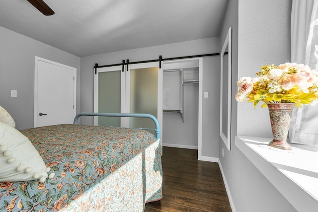 bedroom featuring a barn door, a ceiling fan, baseboards, a closet, and dark wood finished floors