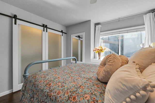 bedroom featuring a textured ceiling, a barn door, wood finished floors, a ceiling fan, and baseboards