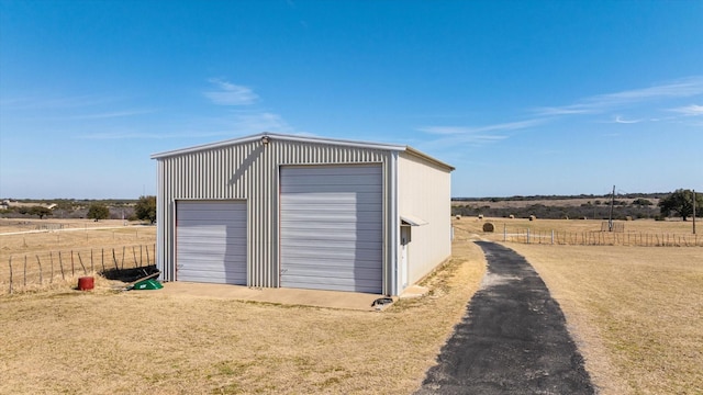 detached garage featuring a rural view and fence