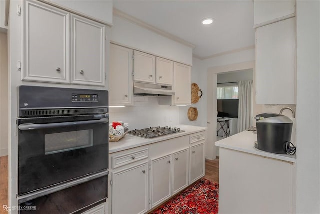 kitchen with under cabinet range hood, stainless steel gas cooktop, black oven, light countertops, and a warming drawer