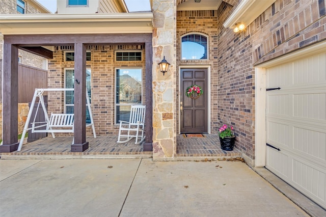 entrance to property featuring a garage, covered porch, and brick siding