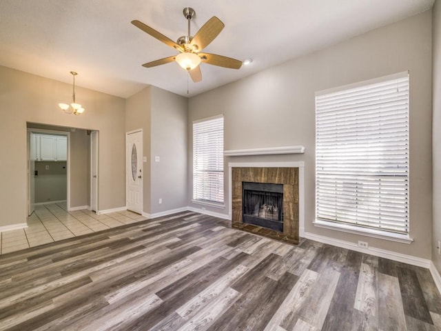 unfurnished living room with ceiling fan with notable chandelier, a tile fireplace, baseboards, and wood finished floors