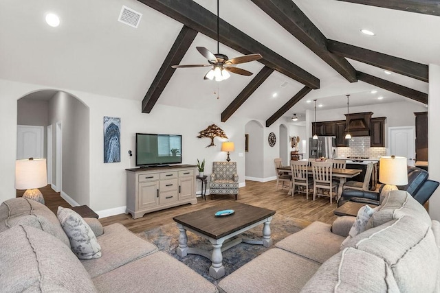 living area with visible vents, vaulted ceiling with beams, baseboards, light wood-style flooring, and arched walkways