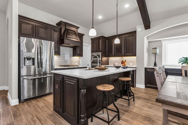 kitchen with light wood finished floors, stainless steel appliances, dark brown cabinetry, custom range hood, and light countertops