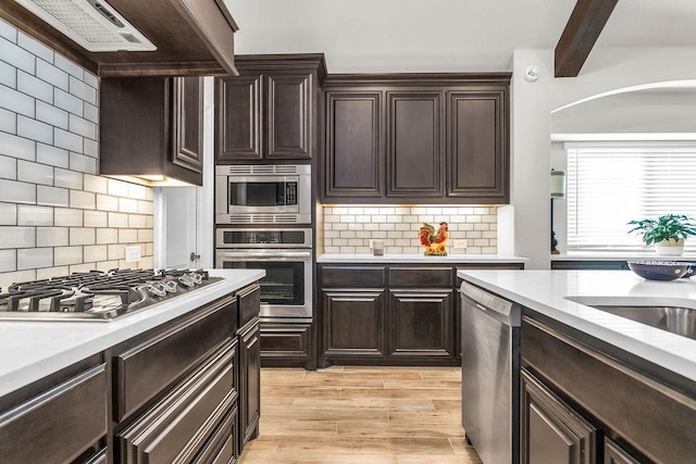 kitchen with beamed ceiling, appliances with stainless steel finishes, light countertops, and wall chimney range hood