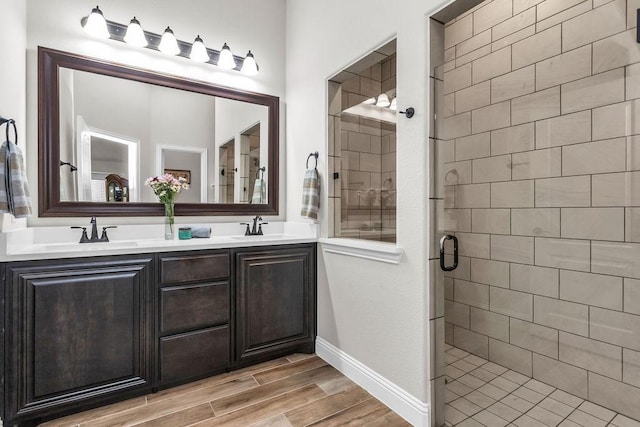 bathroom featuring double vanity, wood finish floors, a stall shower, and a sink