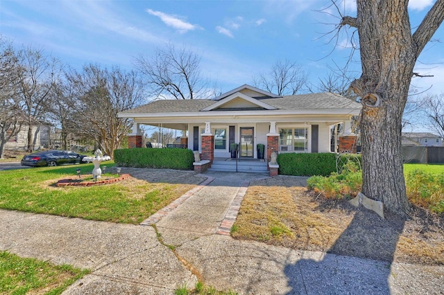 bungalow-style house with brick siding, roof with shingles, a porch, and a front yard