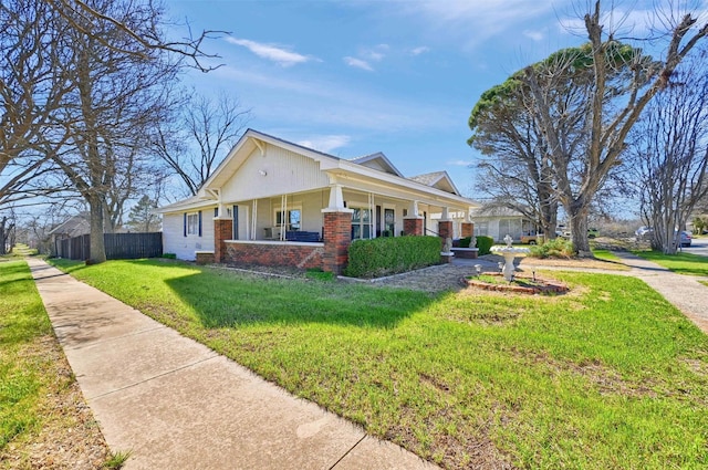 view of side of property featuring a yard, a porch, fence, and brick siding