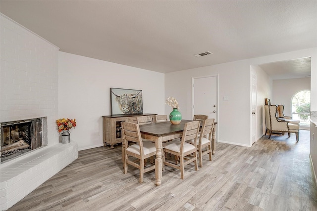 dining space with a brick fireplace, visible vents, light wood-style flooring, and baseboards