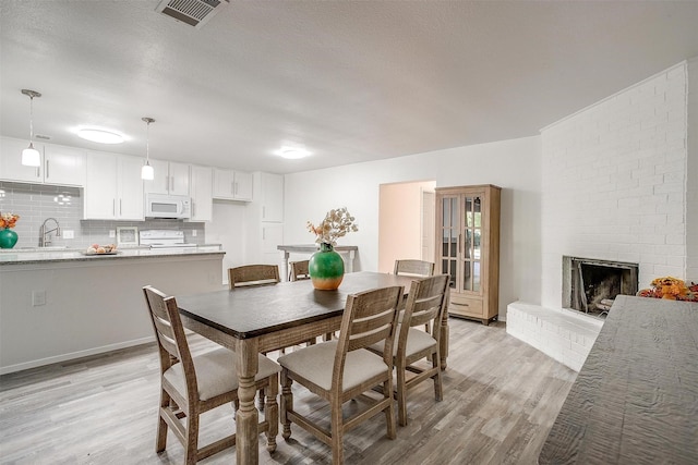 dining space with light wood-style floors, a brick fireplace, visible vents, and a textured ceiling