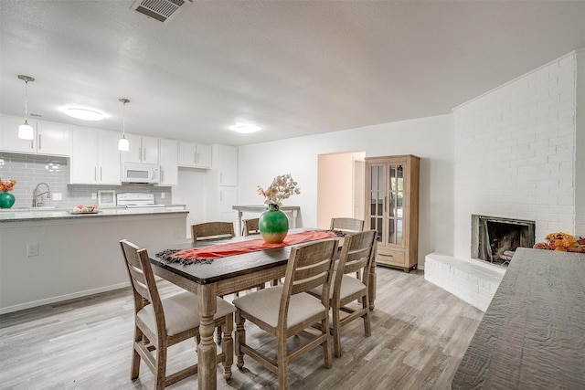 dining area with a textured ceiling, a fireplace, visible vents, and light wood-style floors