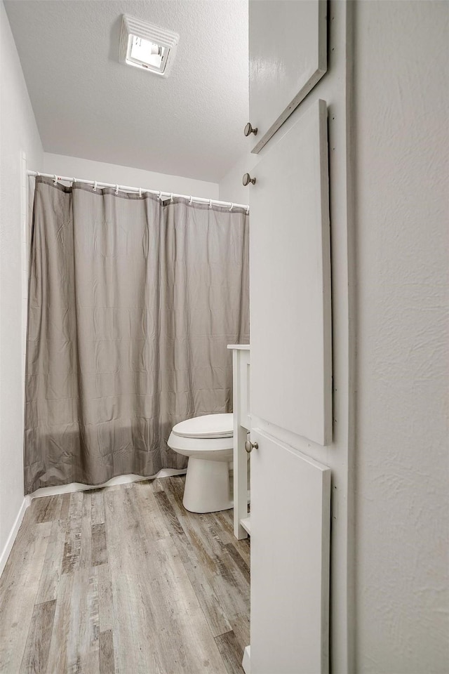 full bath featuring visible vents, toilet, a shower with curtain, wood finished floors, and a textured ceiling