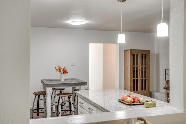 kitchen featuring light stone countertops, white cabinetry, and pendant lighting