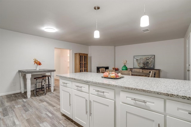 kitchen featuring light wood-style floors, pendant lighting, white cabinetry, and light stone counters