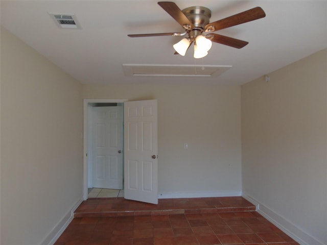 tiled empty room with a ceiling fan, attic access, visible vents, and baseboards