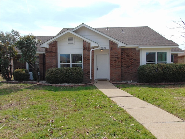 view of front facade with a shingled roof, a front yard, and brick siding